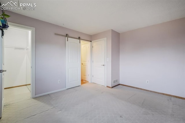 unfurnished bedroom with a barn door, light carpet, and a closet