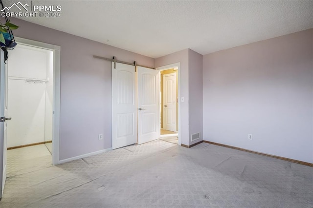 unfurnished bedroom with a barn door, light carpet, a closet, and a spacious closet