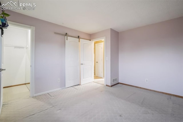 unfurnished bedroom featuring light carpet, a barn door, and a closet