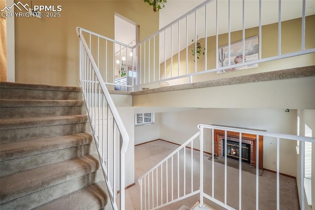 staircase featuring a fireplace and a high ceiling