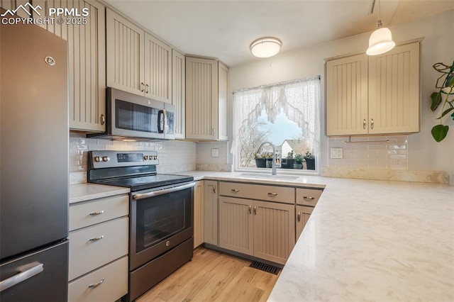 kitchen with pendant lighting, sink, decorative backsplash, appliances with stainless steel finishes, and light hardwood / wood-style floors