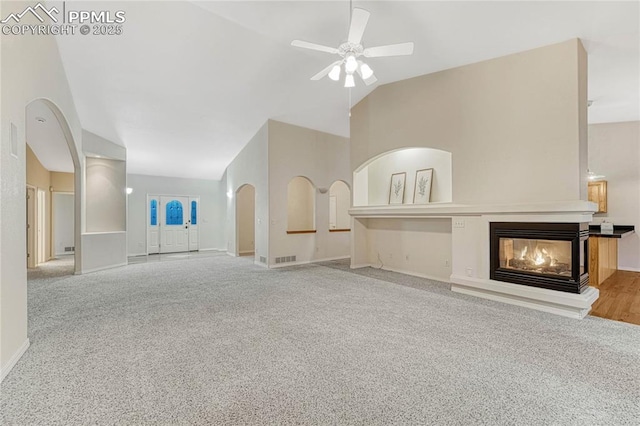 unfurnished living room featuring vaulted ceiling, ceiling fan, a multi sided fireplace, and light carpet