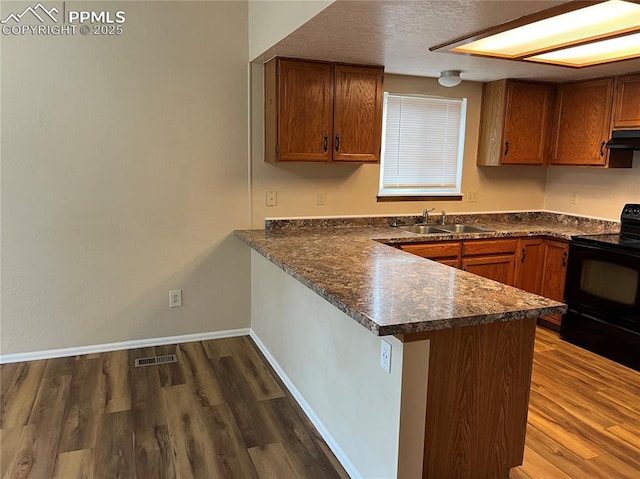 kitchen with kitchen peninsula, extractor fan, sink, dark hardwood / wood-style floors, and black / electric stove