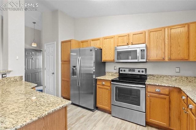 kitchen featuring pendant lighting, vaulted ceiling, light stone countertops, appliances with stainless steel finishes, and light hardwood / wood-style floors