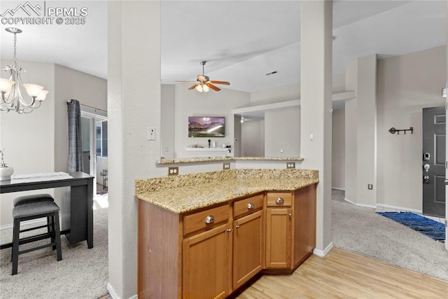 kitchen featuring light stone counters, light hardwood / wood-style flooring, pendant lighting, vaulted ceiling, and ceiling fan with notable chandelier