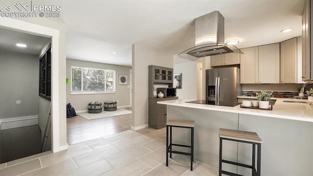 kitchen featuring sink, stainless steel fridge, a kitchen bar, kitchen peninsula, and island exhaust hood