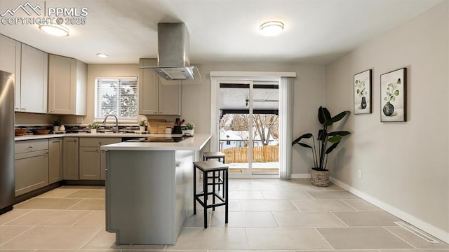 kitchen featuring sink, wall chimney range hood, a breakfast bar area, gray cabinets, and black electric stovetop