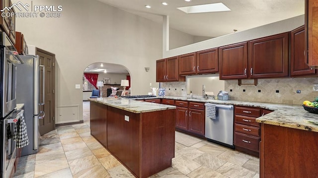 kitchen featuring light stone countertops, appliances with stainless steel finishes, decorative backsplash, a skylight, and high vaulted ceiling