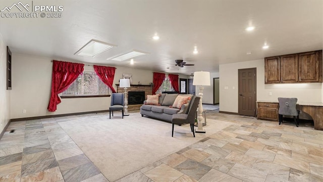 living room with a skylight, ceiling fan, and a stone fireplace