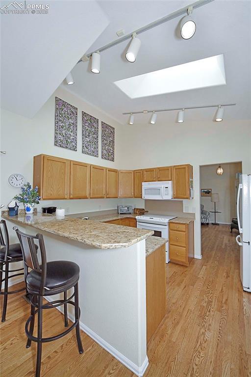 kitchen with a skylight, kitchen peninsula, a towering ceiling, white appliances, and light wood-type flooring