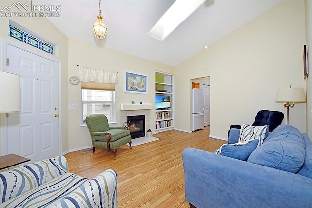 living room featuring a tile fireplace, built in shelves, lofted ceiling with skylight, and hardwood / wood-style floors