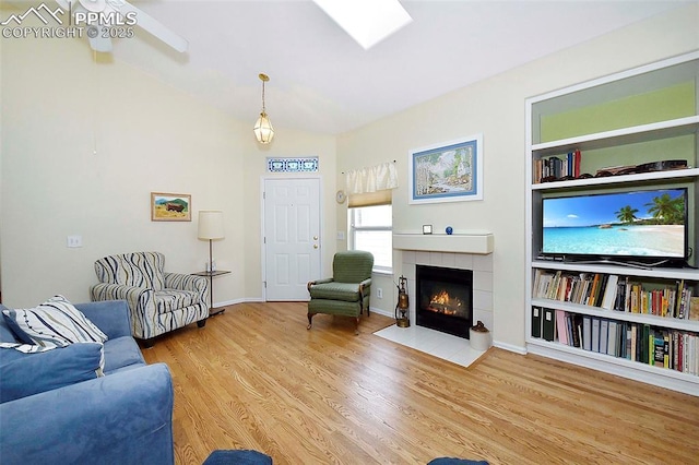 living room featuring a tile fireplace, wood-type flooring, and ceiling fan