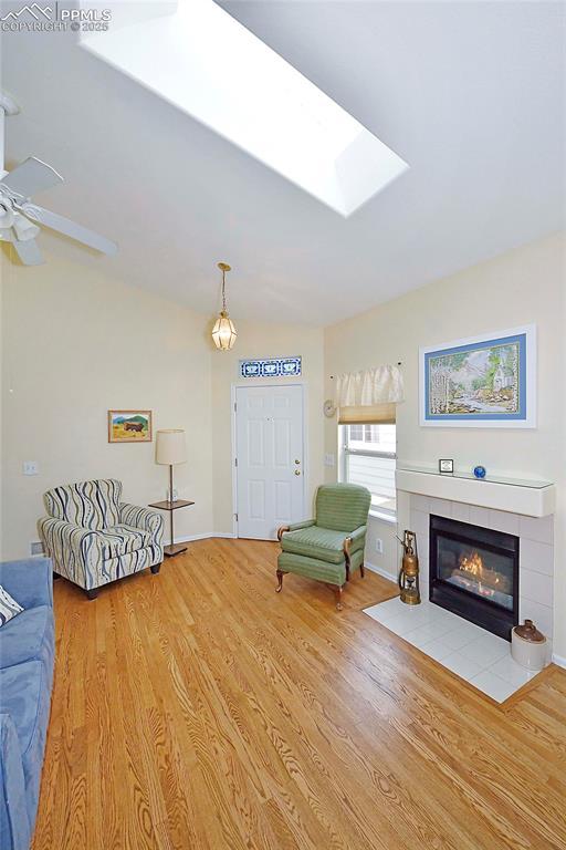 living room with a fireplace, a skylight, ceiling fan, and light hardwood / wood-style floors