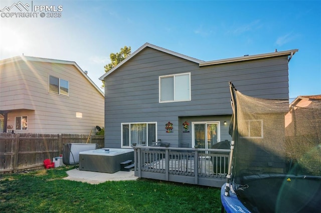 back of house with a yard, a trampoline, a hot tub, and a wooden deck