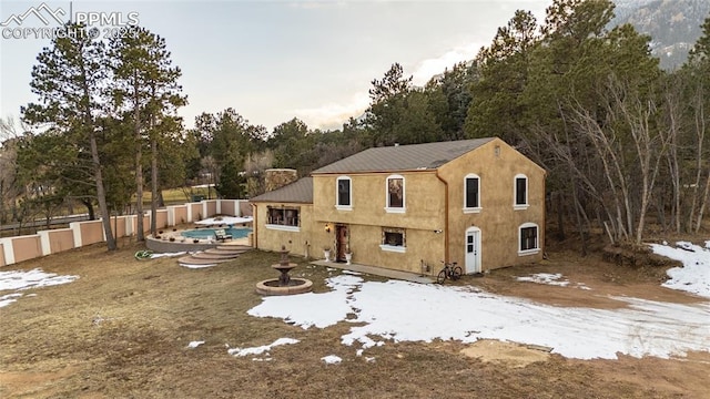 snow covered rear of property with a fenced in pool