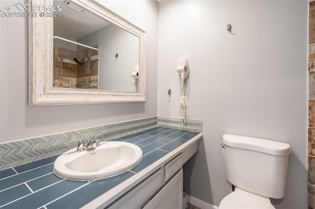 bathroom with tiled shower, vanity, and toilet