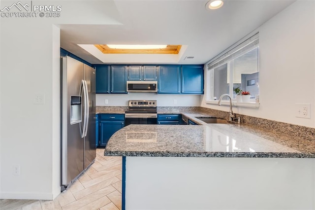 kitchen featuring sink, blue cabinetry, appliances with stainless steel finishes, a tray ceiling, and kitchen peninsula