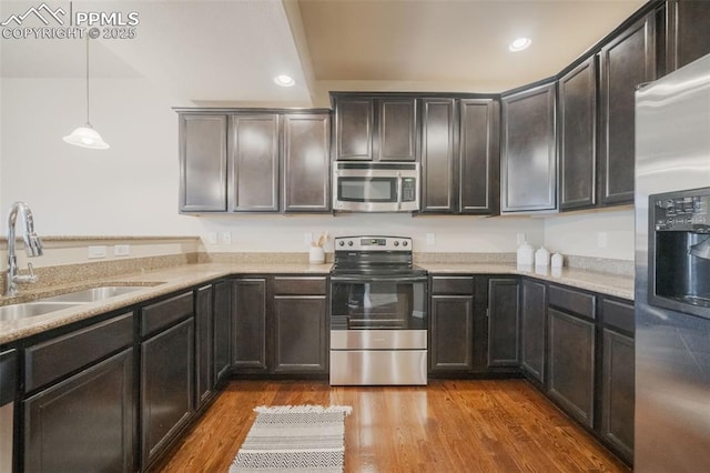 kitchen with hardwood / wood-style floors, sink, decorative light fixtures, light stone counters, and stainless steel appliances