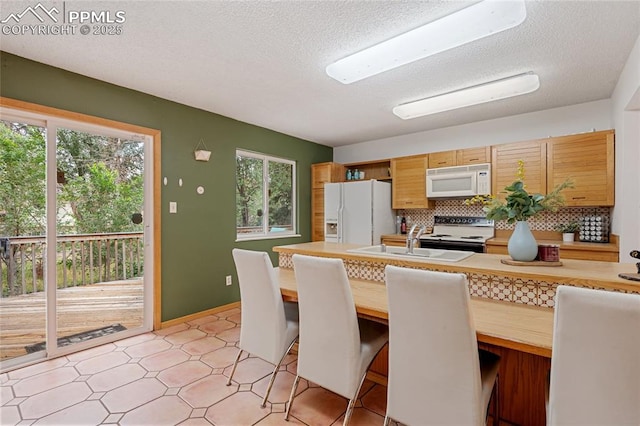 kitchen featuring a kitchen breakfast bar, backsplash, a textured ceiling, white appliances, and sink