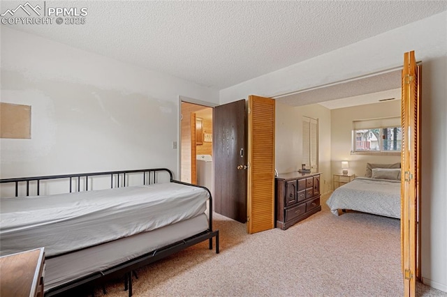 carpeted bedroom with ensuite bathroom, washer / dryer, and a textured ceiling