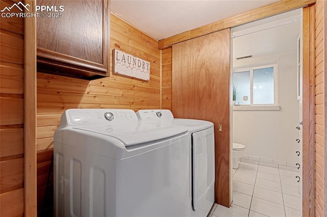 washroom featuring washing machine and clothes dryer, wooden walls, light tile patterned floors, and cabinets