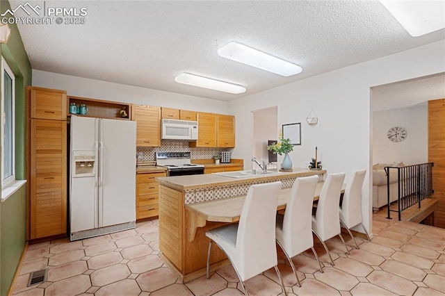 kitchen featuring sink, backsplash, a textured ceiling, white appliances, and a breakfast bar area