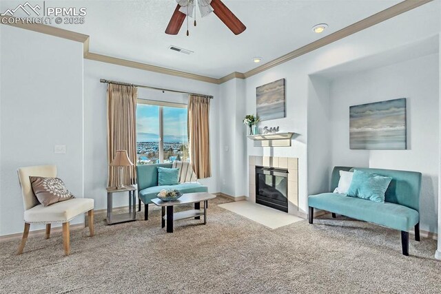 sitting room with a tiled fireplace, light colored carpet, ornamental molding, and ceiling fan