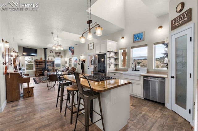 kitchen featuring a wood stove, white cabinets, sink, hanging light fixtures, and appliances with stainless steel finishes