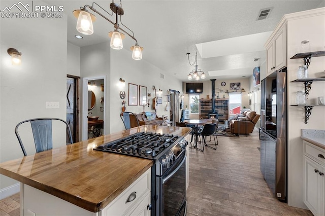 kitchen featuring stainless steel gas range oven, a kitchen island, pendant lighting, light hardwood / wood-style flooring, and white cabinetry