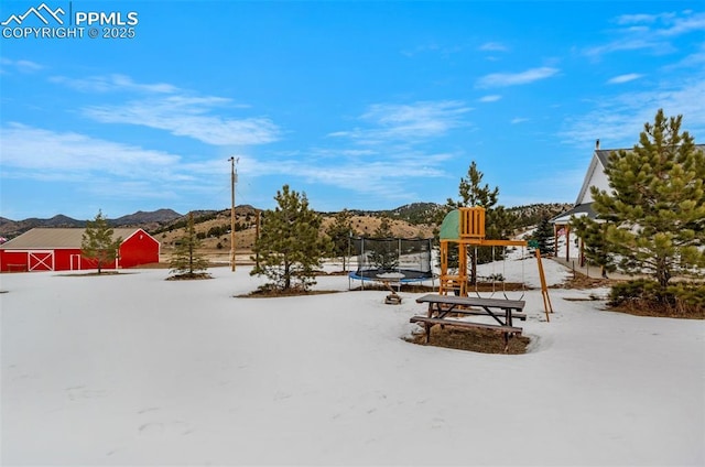 snowy yard with a mountain view and a trampoline