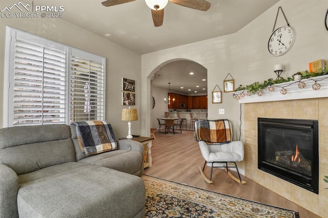 living room with ceiling fan, wood-type flooring, and a tile fireplace