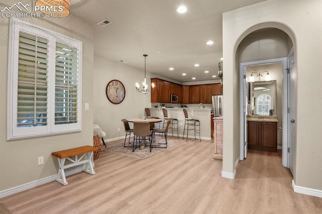 kitchen with stainless steel appliances, sink, pendant lighting, an inviting chandelier, and light hardwood / wood-style floors