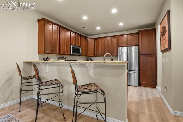 kitchen featuring kitchen peninsula, a kitchen bar, light wood-type flooring, light stone counters, and stainless steel appliances