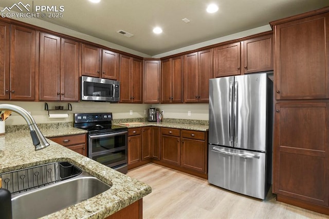 kitchen with sink, light stone countertops, stainless steel appliances, and light hardwood / wood-style flooring