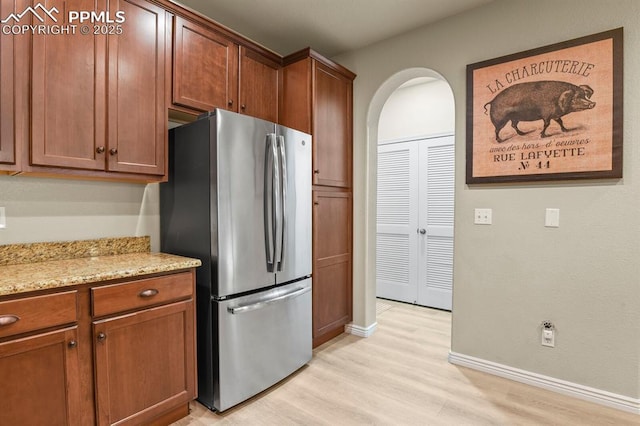 kitchen featuring stainless steel refrigerator, light stone countertops, and light hardwood / wood-style flooring