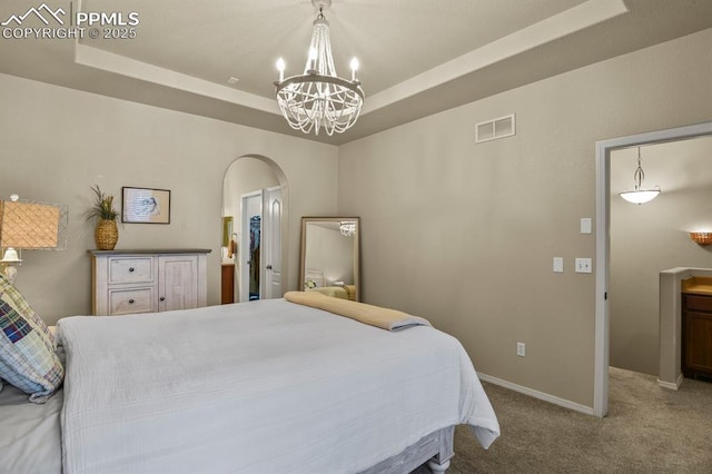 carpeted bedroom featuring a raised ceiling and a chandelier