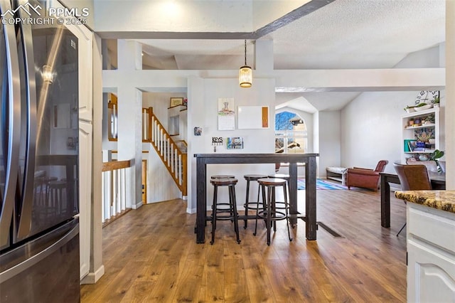 kitchen with decorative light fixtures, vaulted ceiling, wood-type flooring, a textured ceiling, and black refrigerator