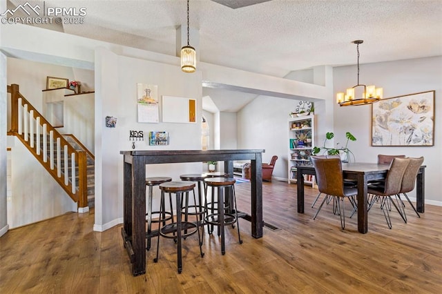 dining space featuring a textured ceiling, a chandelier, lofted ceiling, and hardwood / wood-style flooring