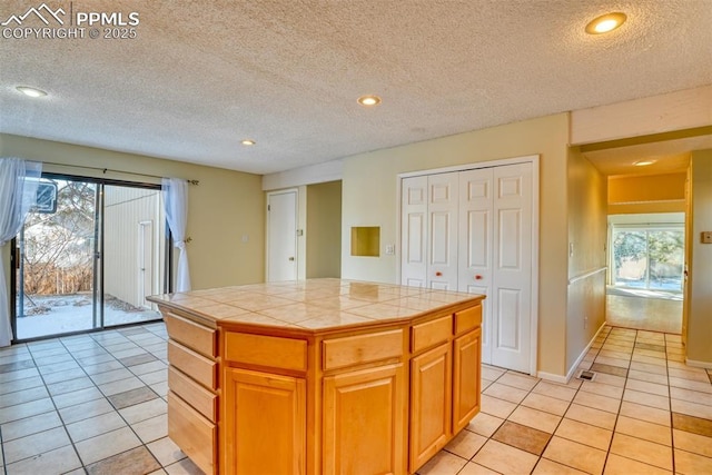 kitchen with tile countertops, a center island, light tile patterned floors, and a textured ceiling