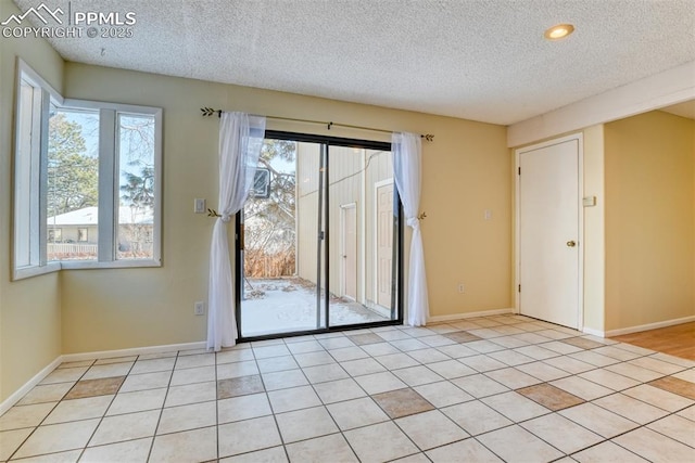 spare room featuring light tile patterned floors, a textured ceiling, and a healthy amount of sunlight