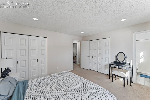 bedroom featuring light colored carpet, a textured ceiling, connected bathroom, and two closets