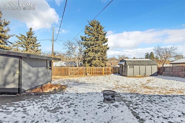 yard layered in snow featuring a storage unit and an outdoor fire pit