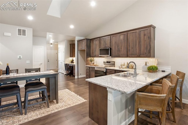 kitchen with kitchen peninsula, appliances with stainless steel finishes, decorative backsplash, light stone counters, and sink