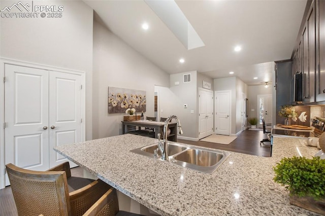 kitchen with stove, sink, light stone counters, dark brown cabinetry, and a breakfast bar area