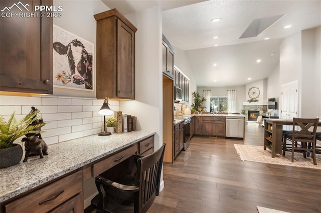 kitchen with stainless steel appliances, tasteful backsplash, light stone counters, dark hardwood / wood-style floors, and vaulted ceiling