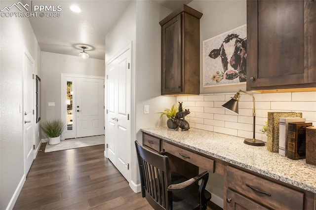 kitchen featuring light stone countertops, built in desk, backsplash, and dark brown cabinetry