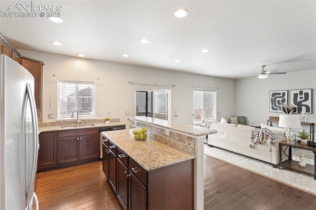 kitchen with dark hardwood / wood-style flooring, light stone counters, sink, a center island, and white fridge