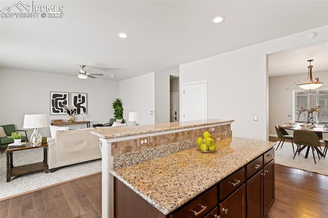 kitchen with ceiling fan, a center island, dark hardwood / wood-style flooring, and light stone counters