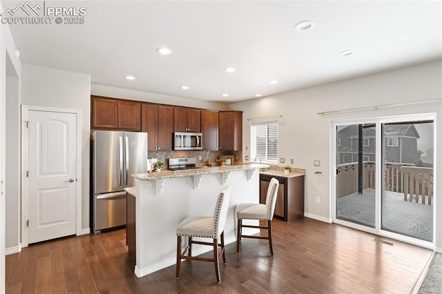 kitchen with a kitchen bar, light stone countertops, tasteful backsplash, stainless steel appliances, and a center island