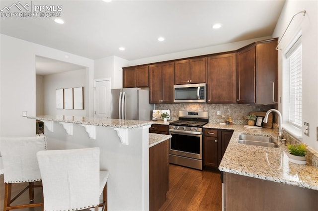 kitchen with sink, a center island, stainless steel appliances, light stone counters, and a kitchen bar